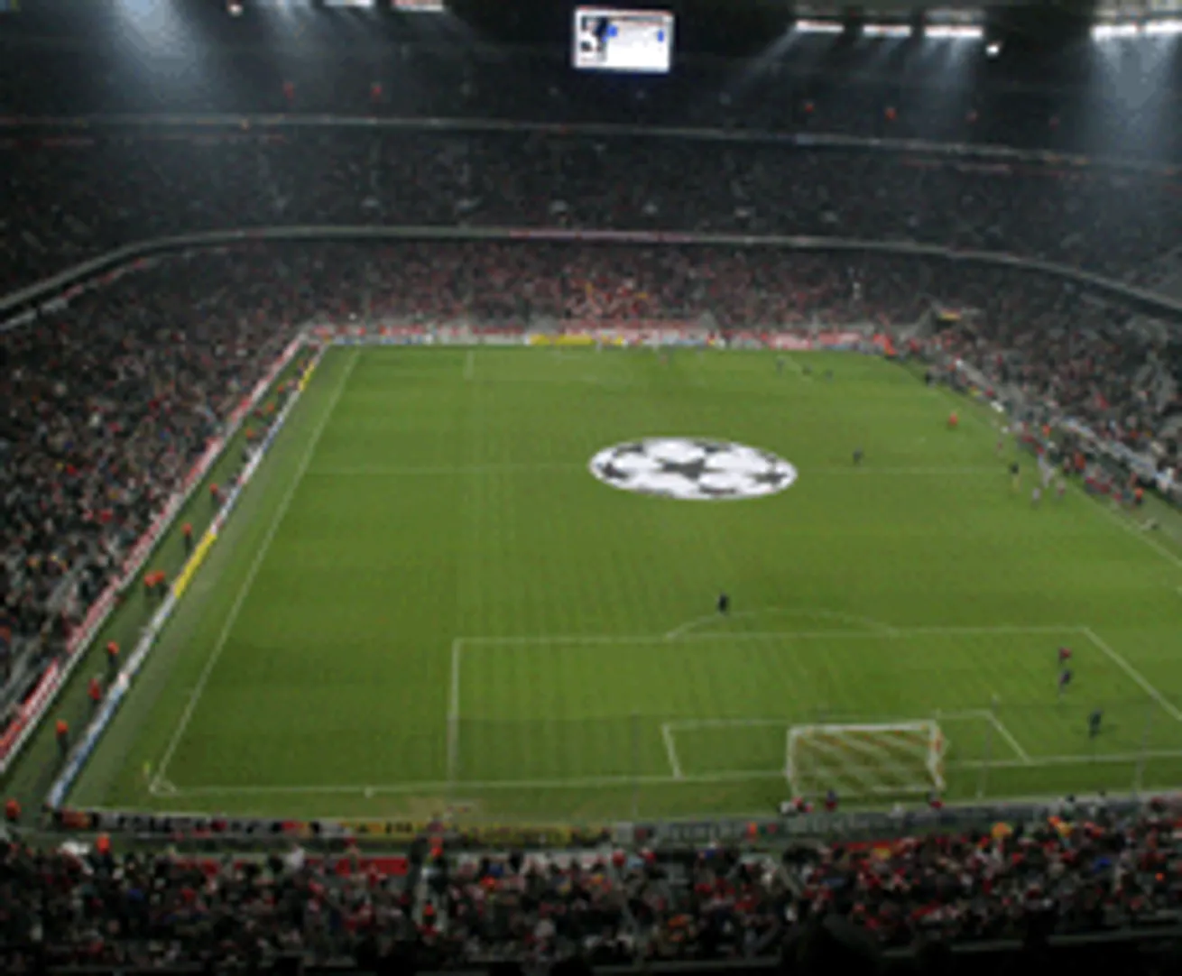 A football stadium with a large display screen and a logo at the center of the field.