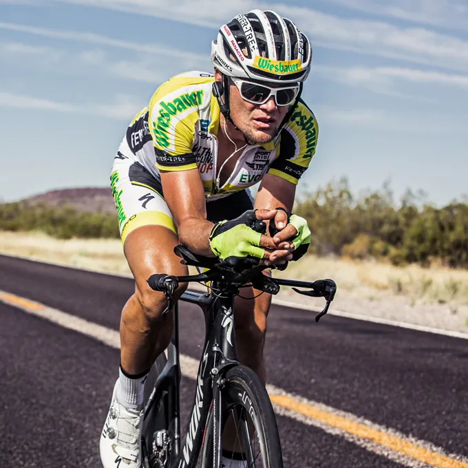 A cyclist in a yellow and black jersey and gloves rides on a road, wearing a special cycling helmet and sunglasses.