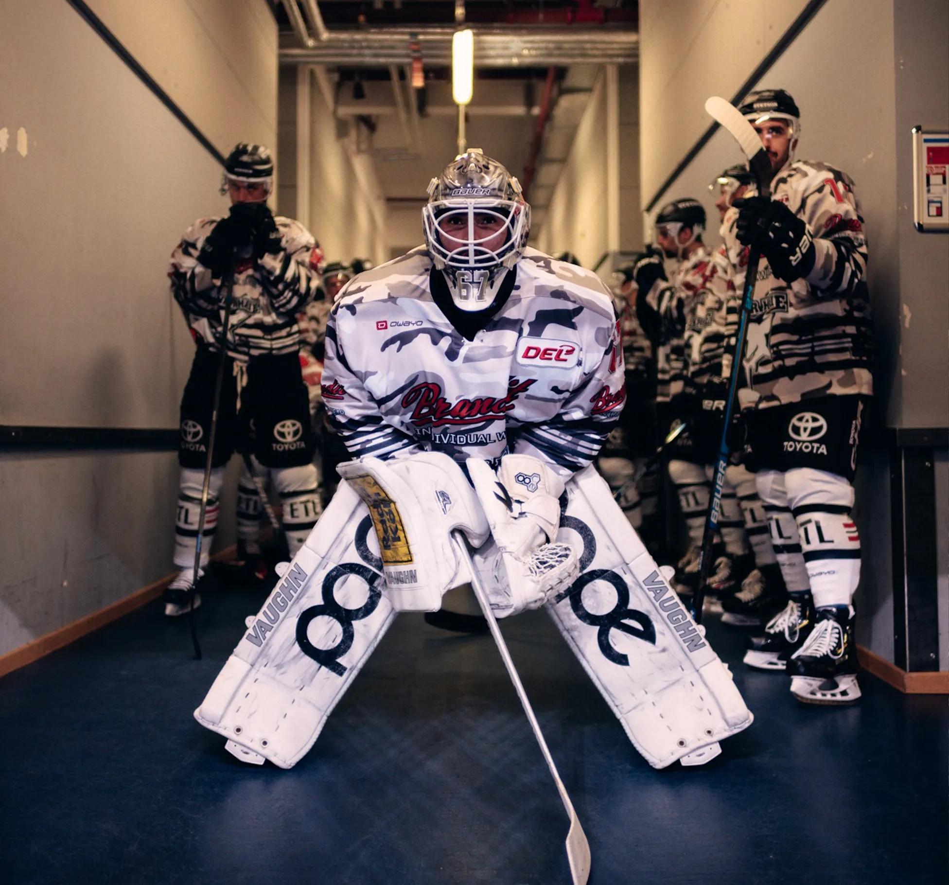 A hockey goalie in a striking uniform stands ready, while other players wait behind him.