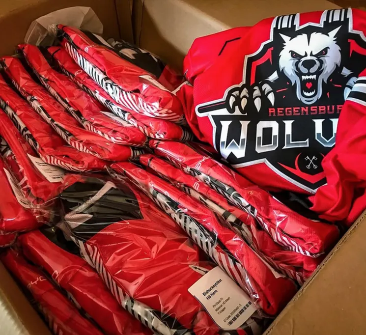 A cardboard box filled with several red, custom-printed sports jerseys wrapped in plastic, one featuring a wolf logo and the text 'REGENSBURG WOLVES'.