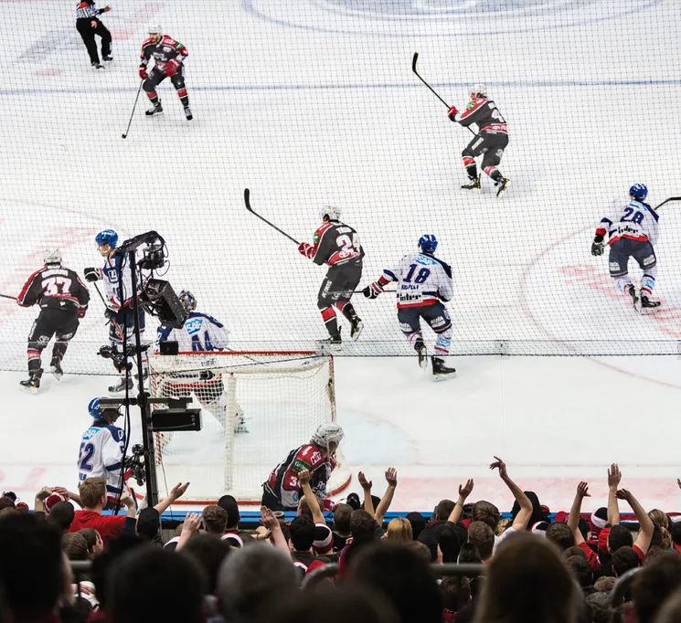 A dynamic ice hockey scene featuring players in action on the ice with a cheering crowd in the background.