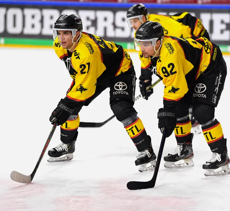 Hockey players in yellow and black jerseys with numbers 21 and 92 on the ice, holding their sticks.