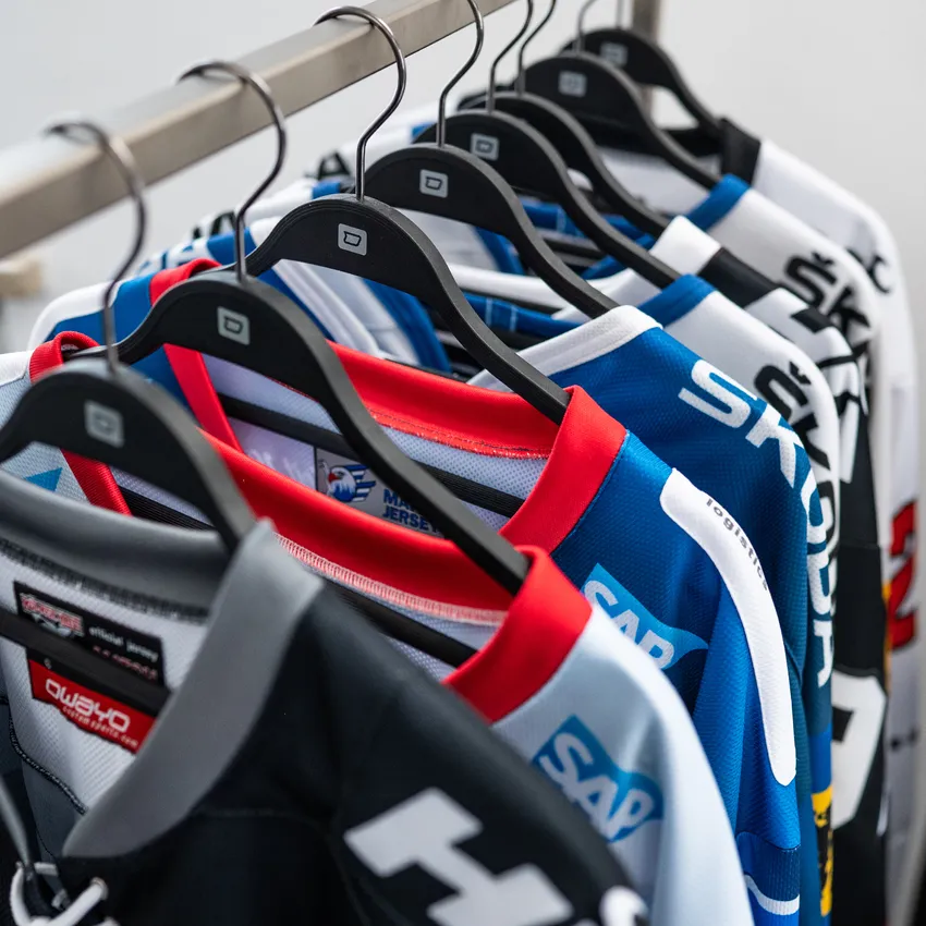 A row of various colored sports jerseys hanging on a hanger.
