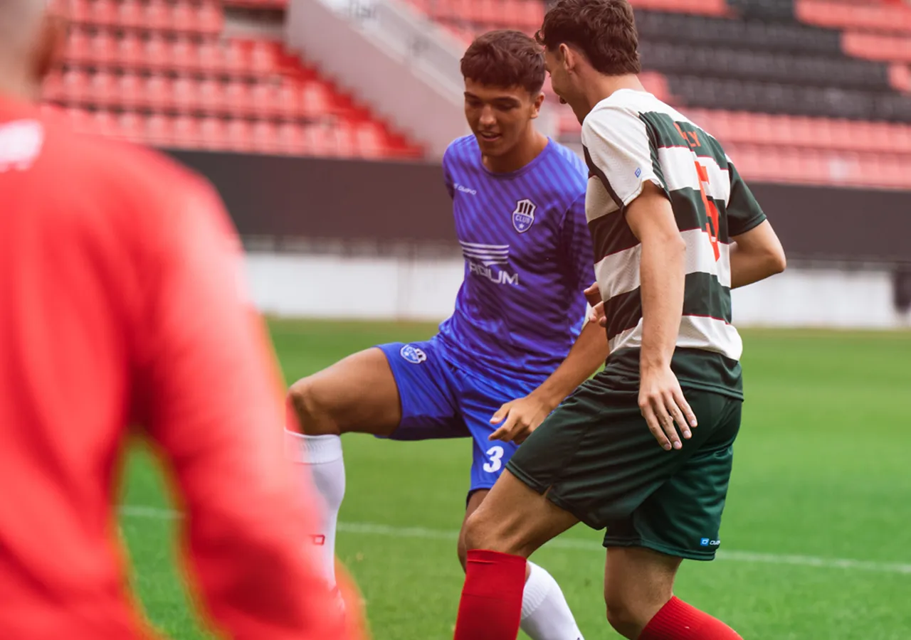 Two soccer players in action on the field, one wearing a blue jersey and the other in a green and white striped jersey.