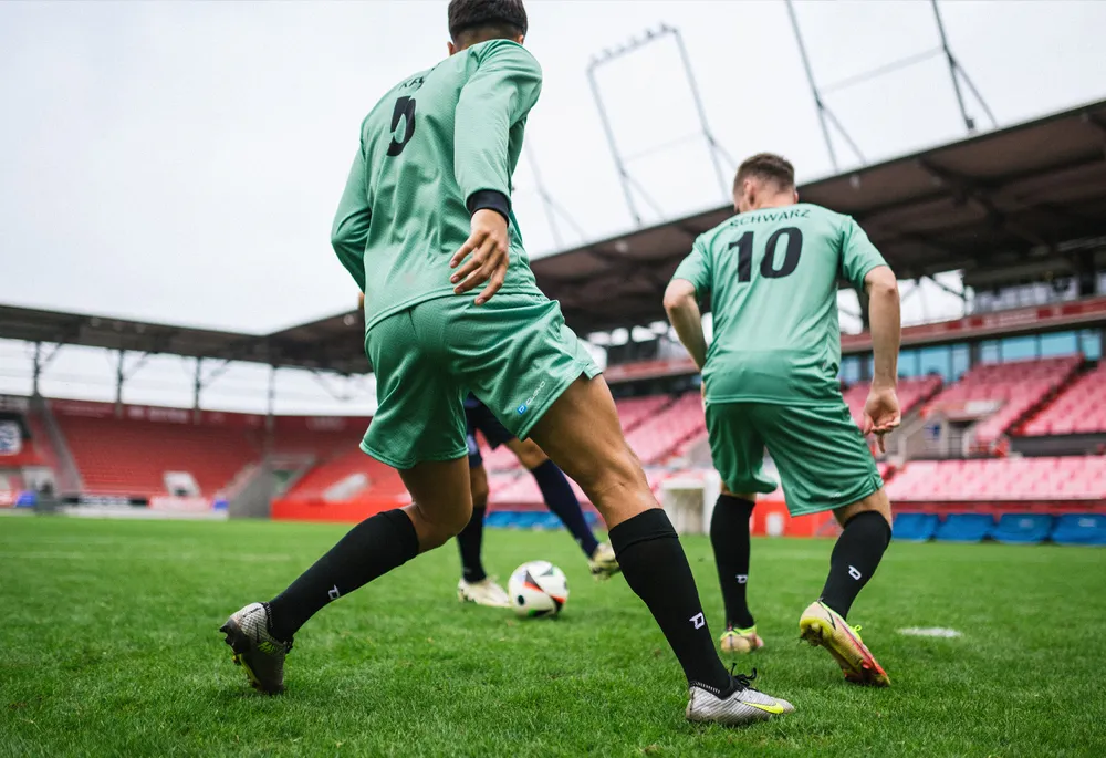 Two soccer players in green jerseys and black socks playing on a grass field.