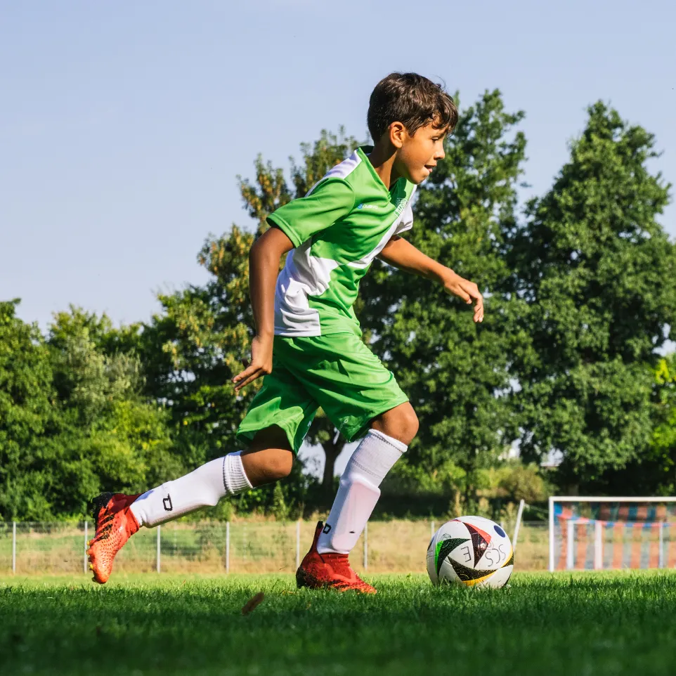 A young soccer player in green and white sportswear runs on a soccer field.