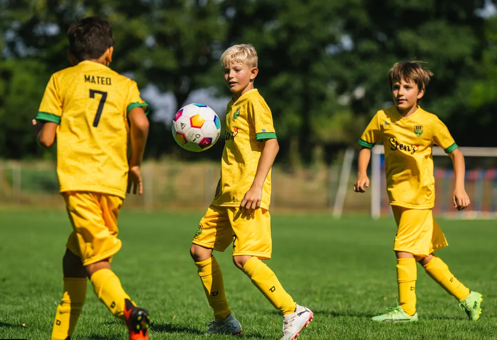 Three children in bright yellow soccer jerseys are playing on a grassy field.