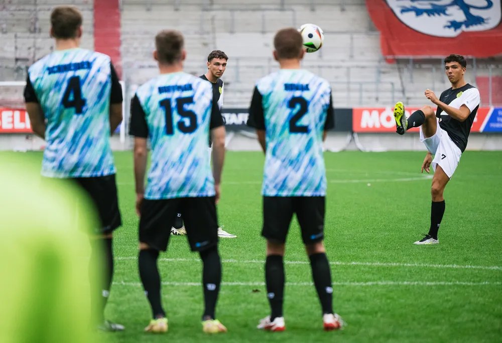 A group of soccer players in colorful jerseys stands on the field while one player prepares to take a free kick.