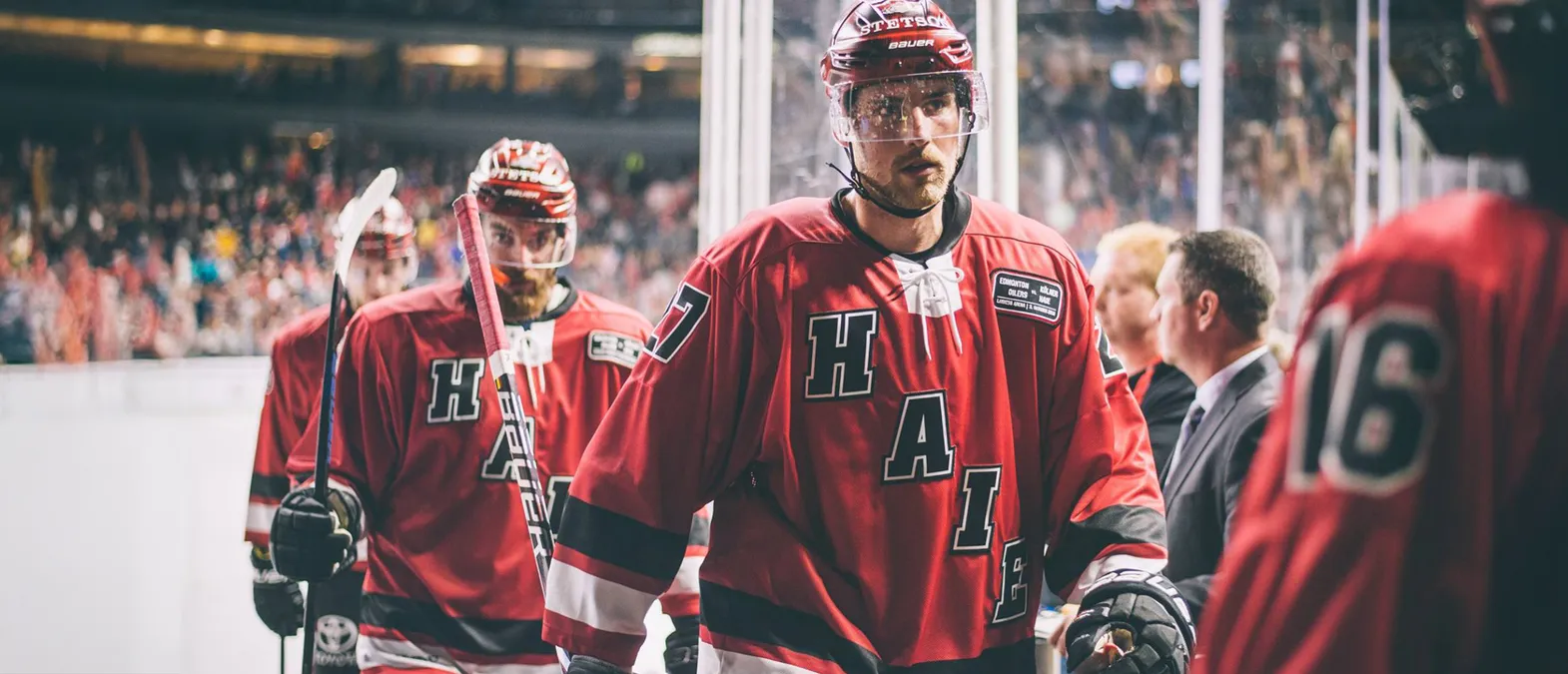 Hockey players in red jerseys with the letters 'H', 'A', 'I', 'E' and the number 7 on the back, standing on the ice.