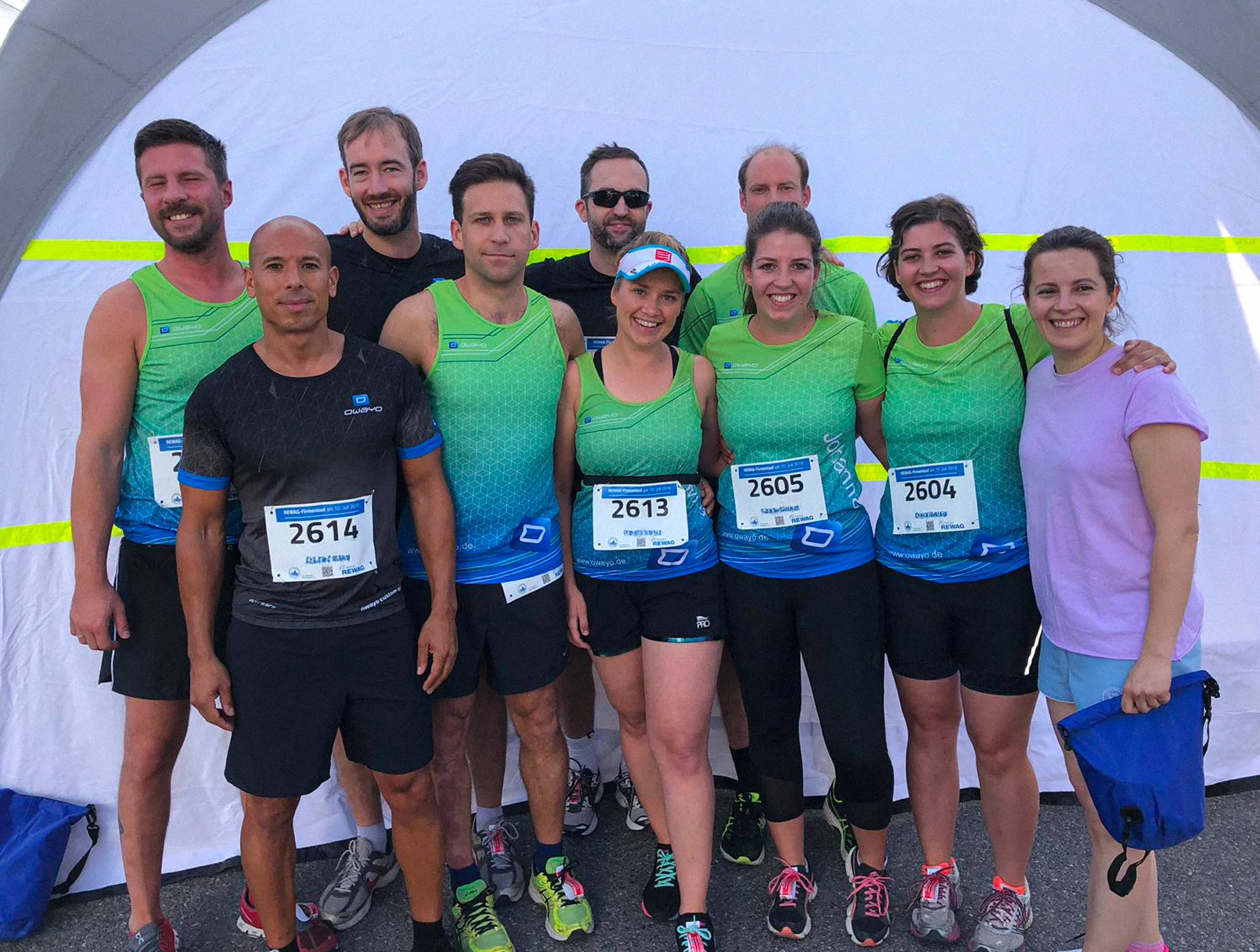 A group of runners in customized sportswear from owayo pose in front of a tent, some wearing race numbers.
