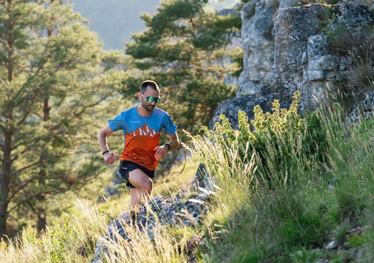 A runner in colorful sportswear navigating rocky terrain in a forested area.