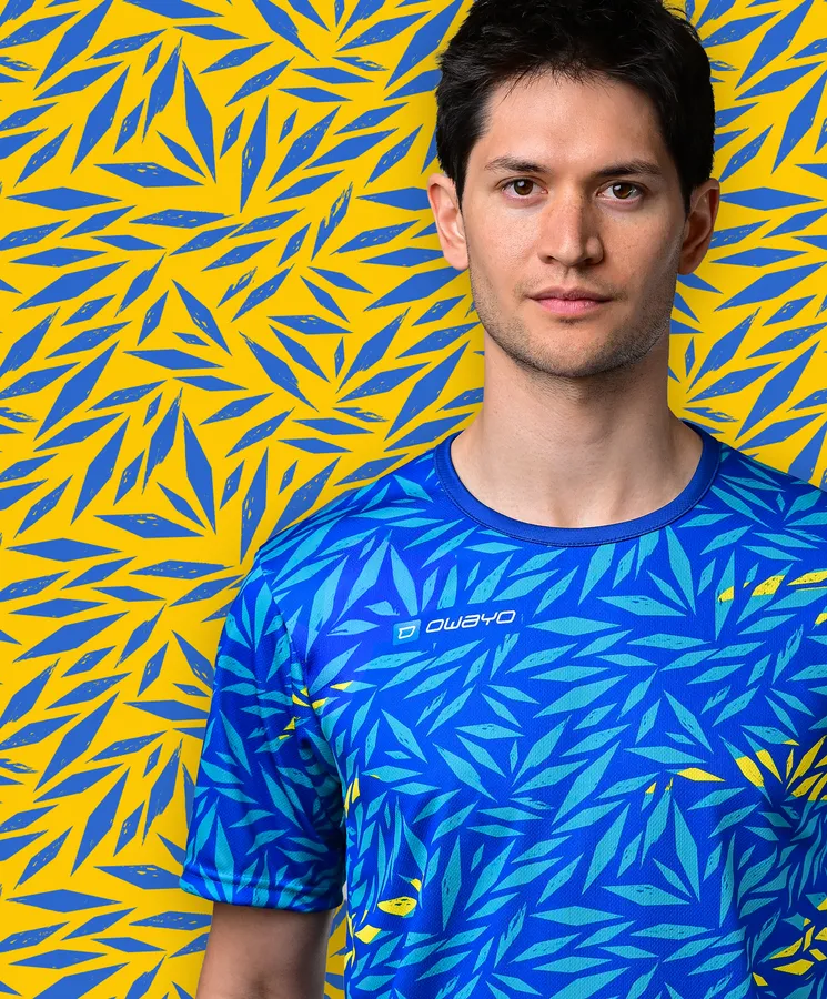 A young man is wearing a sporty blue T-shirt featuring a colorful leaf pattern against a yellow background.