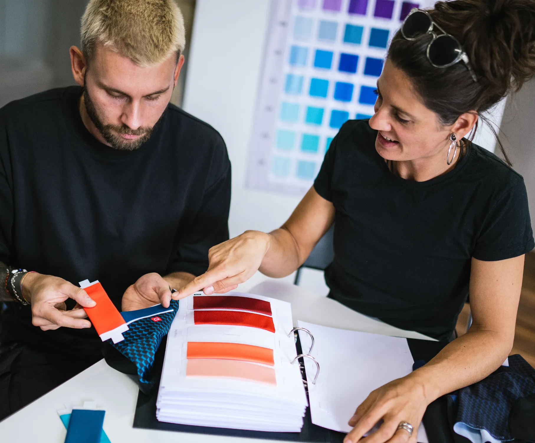 A man and a woman select colors for customized sportswear, examining fabric swatches and color samples.
