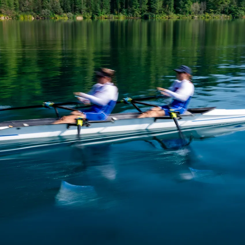 Two rowers in blue sportswear making powerful strokes on a calm lake.