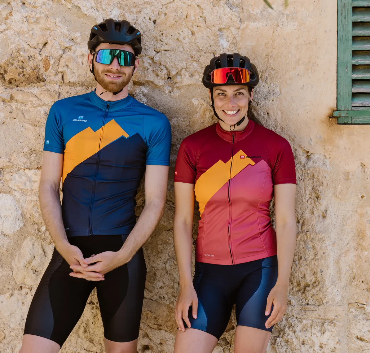 A man and a woman in customized cycling jerseys from owayo, standing in front of a stone wall.